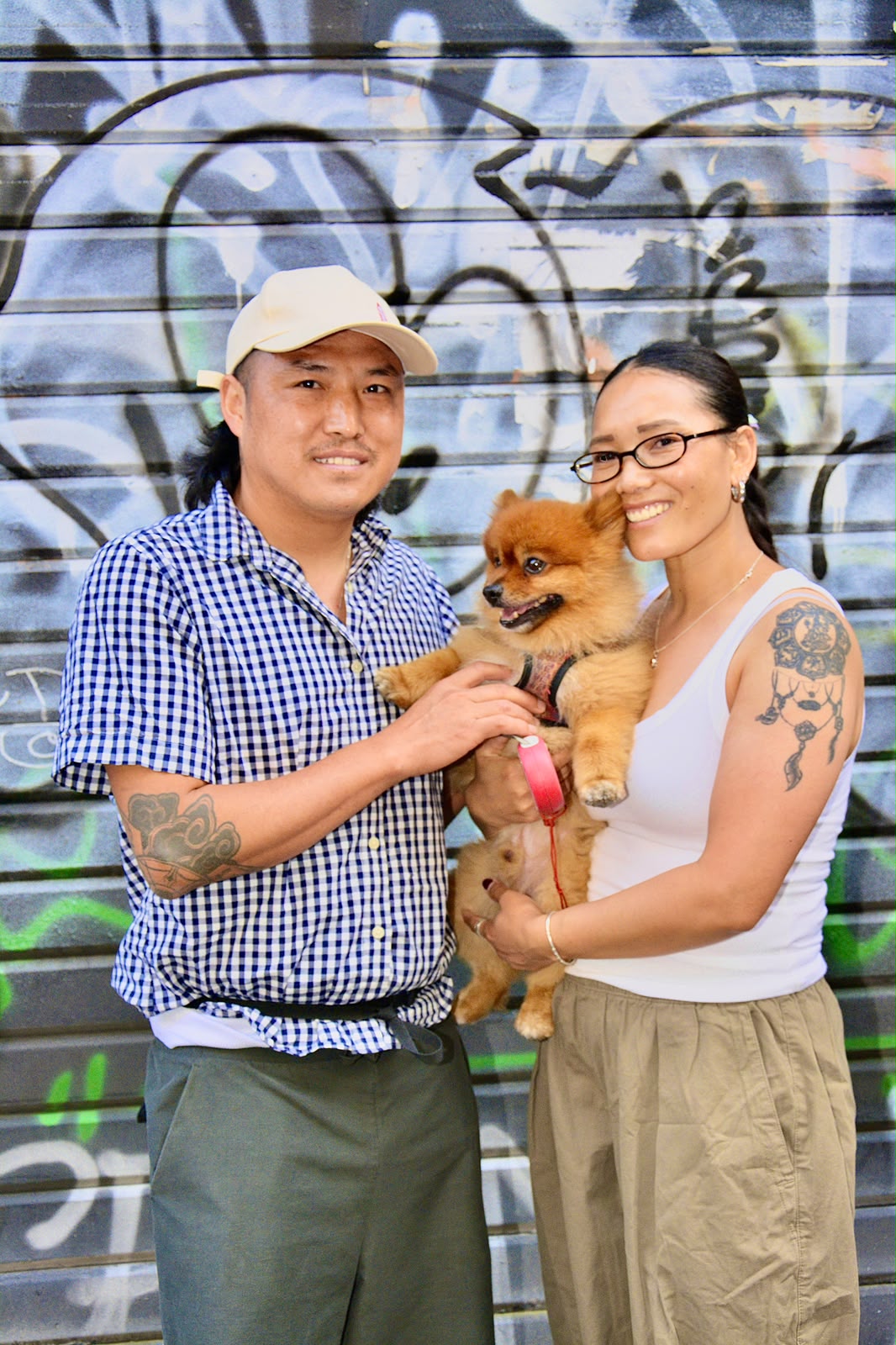 Couple souriant tenant un chien loulou de Poméranie devant un rideau métallique couvert de graffitis