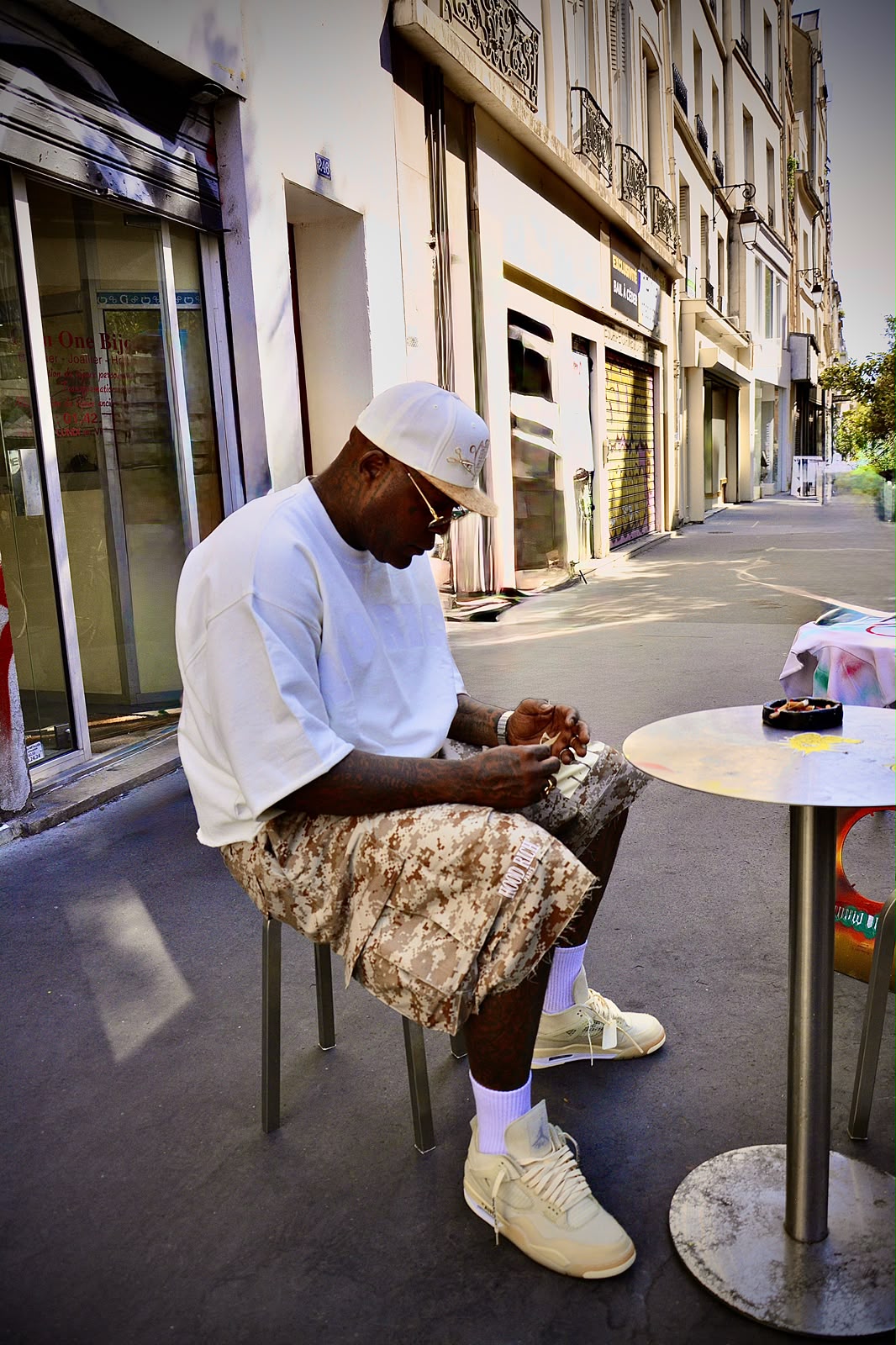 Homme assis à une table haute en terrasse dans une rue parisienne, de profil, sous une forte lumière d'été