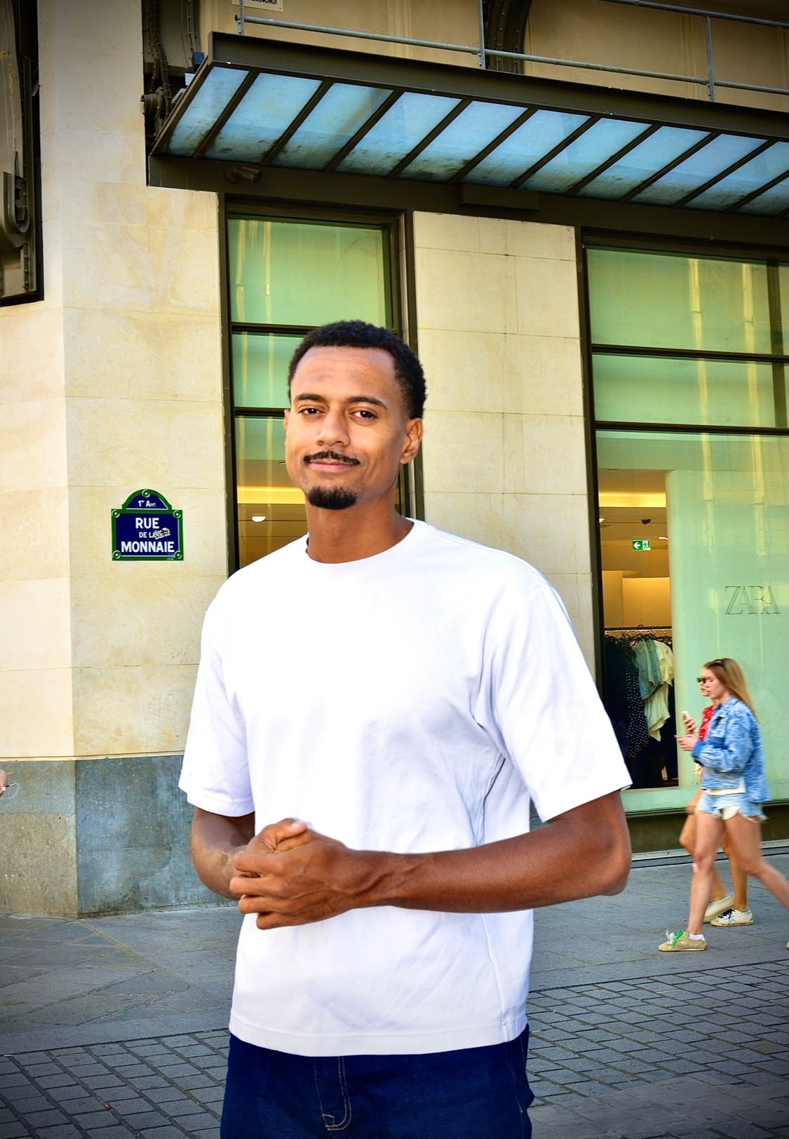 Portrait de rue d'un homme en t-shirt blanc devant une vitrine, rue de la Monnaie