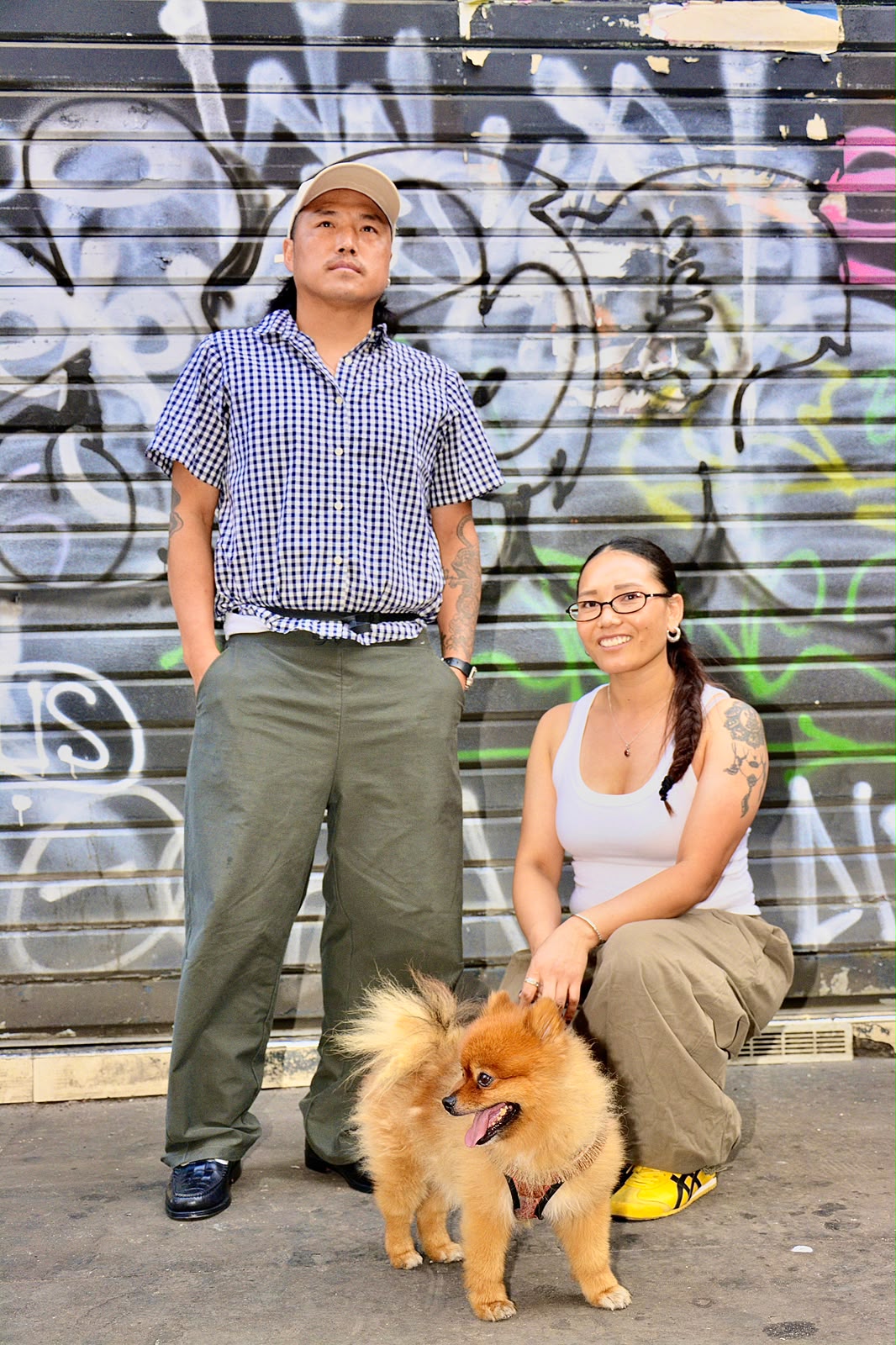 Couple posant avec son chien loulou de Poméranie devant un rideau métallique couvert de graffitis en noir et blanc